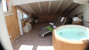 An attic bedroom with a hot tub, two lounge chairs, and a window. - Miralago (Tremosine)