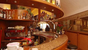 A bar area with a curved counter, shelves with bottles, a coffee machine, and a mirror reflecting the interior. - Miralago (Tremosine)