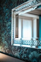 Un miroir avec un cadre décoratif, placé devant un papier peint à motifs floraux.