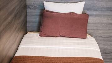 Un lit avec une couverture marron, un oreiller blanc et un autre oreiller marron.