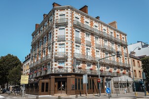 Un immeuble d’angle abritant un hôtel au rez-de-chaussée, caractérisé par une façade traditionnelle en briques et de nombreux balcons.