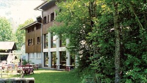 Een gebouw met een houten gevel en grote ramen, omgeven door weelderige begroeiing.