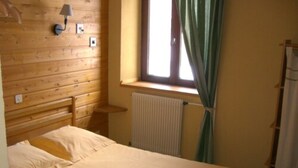 Een slaapkamer met een houten hoofdeinde, een enkel bed, een nachtkastje, een wandlamp, een raam met gordijnen en een radiator.