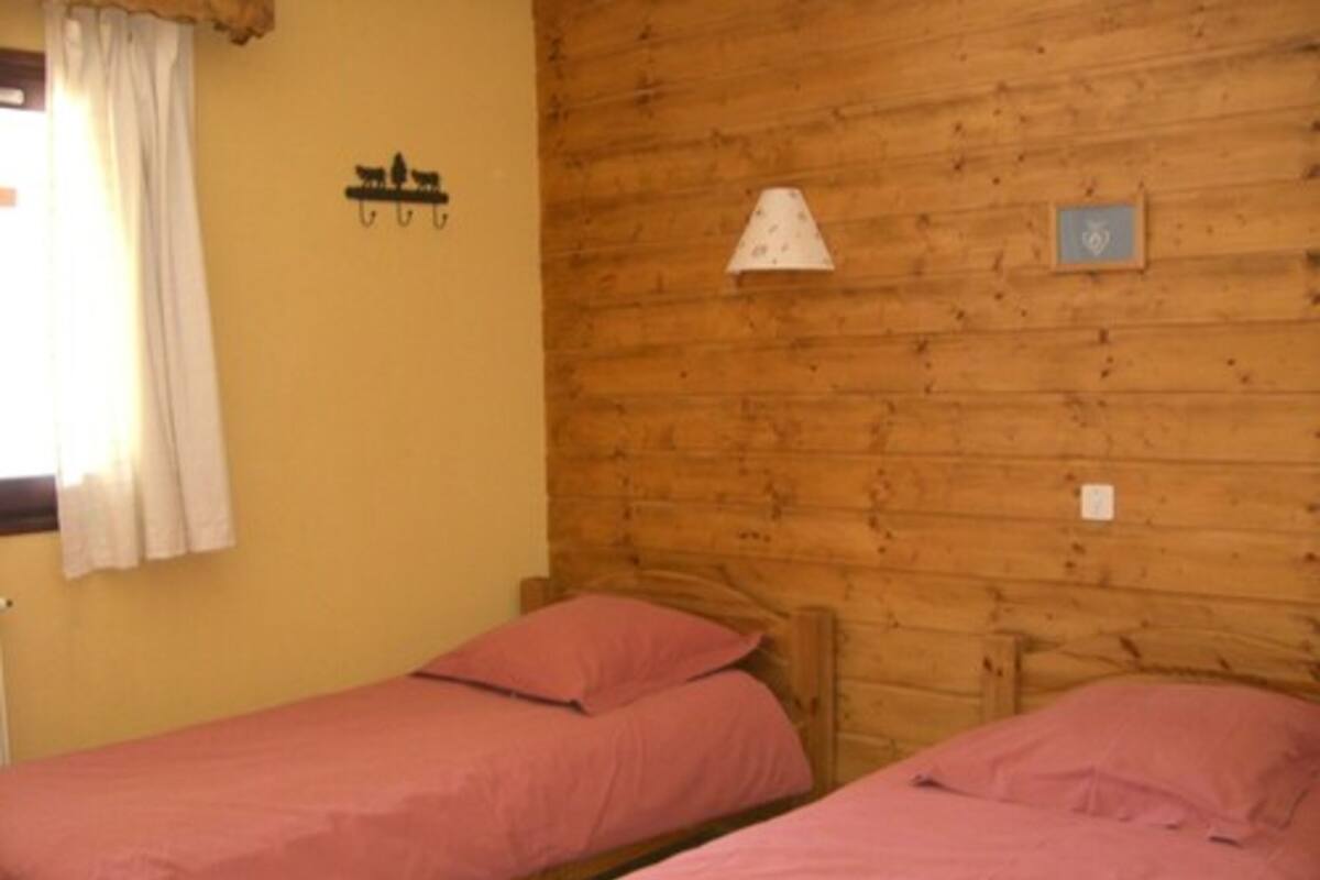 Una stanza con due letti a castello in legno, una finestra con tende bianche, una lampada fissata al muro e un piccolo quadro incorniciato.
