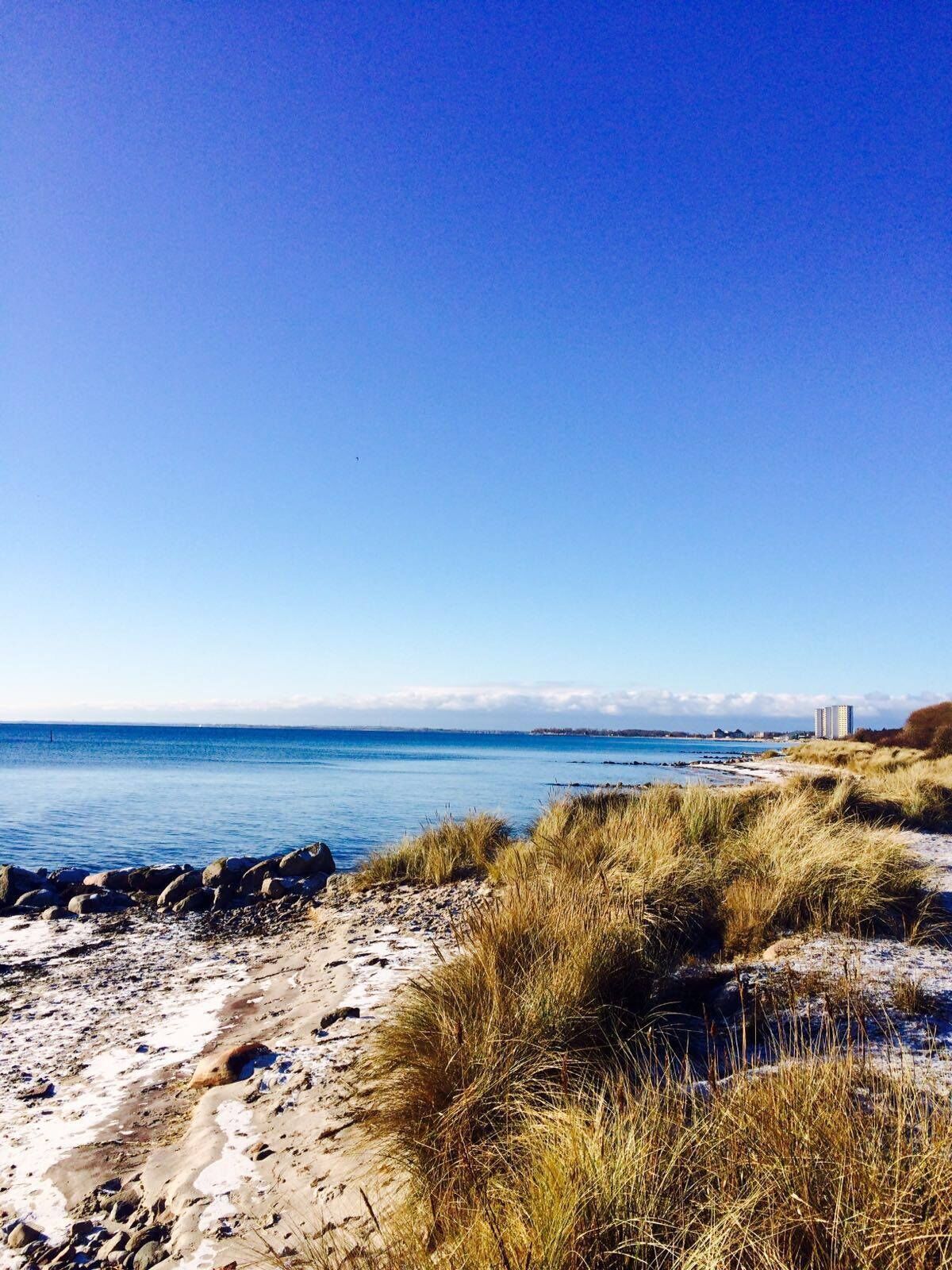 A beach with a clear sky, a rocky shoreline, and a distant building.