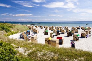 A beach with numerous wooden huts arranged in rows, some with colorful canopies, and a clear view of the sea and boats in the distance. - Strandhotel Bene (Fehmarn)