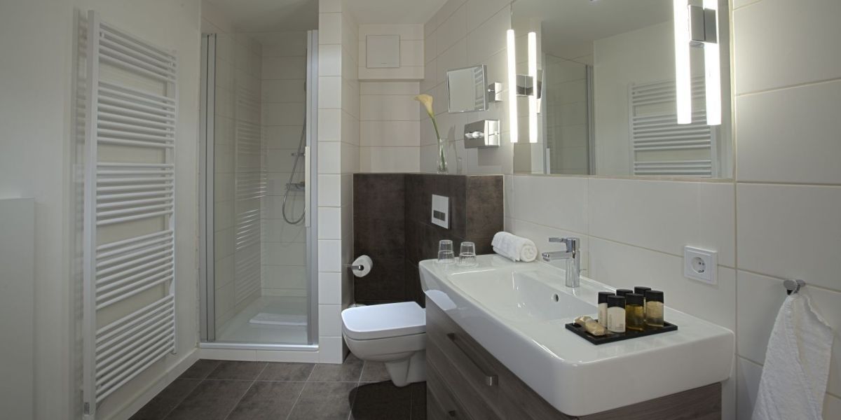 Un baño moderno con cabina de ducha de vidrio, inodoro blanco, tocador grande con espejo y perchero para toallas.