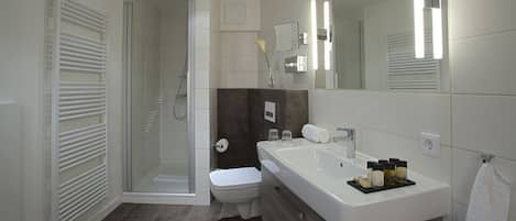 Un baño moderno con cabina de ducha de vidrio, inodoro blanco, tocador grande con espejo y perchero para toallas.