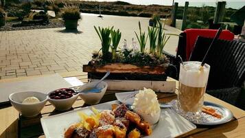A table with a plate of food, a glass of a beverage, and a bowl of cherries.