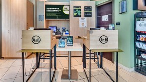 Zona de recepción de un hotel B&B con mobiliario de madera, una pantalla digital y una máquina expendedora de snacks.