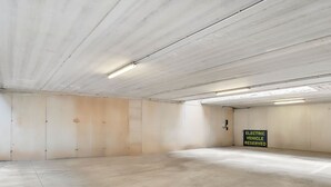 Un estacionamiento vacío con paredes y pisos de concreto, iluminación fluorescente y un letrero que dice 'Vehículo Eléctrico Reservado'.