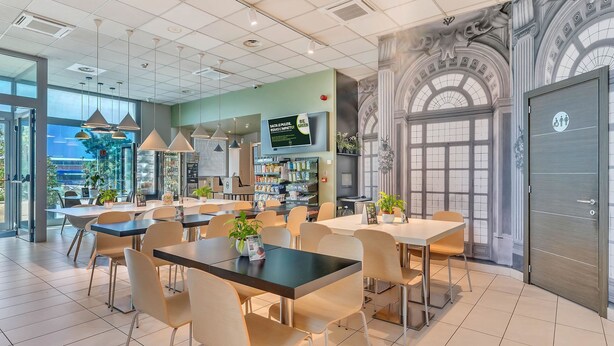 Una cafetería moderna con varias zonas de estar, incluyendo mesas y sillas, y una barra con un menú.