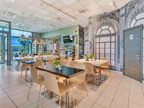 Una cafetería moderna con varias zonas de estar, incluyendo mesas y sillas, y una barra con un menú.
