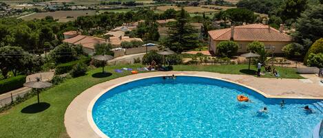A large, curved swimming pool surrounded by a well-maintained lawn and a few umbrellas.