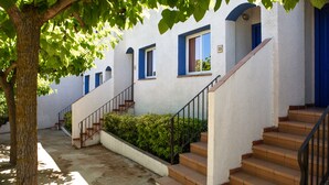 A building with white walls, blue doors, and windows, featuring a staircase and a tree in the foreground. -  RVApartaments Club Torrevella (Torroella de Montgrí)