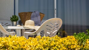 A patio with white plastic chairs and a table, a potted plant, and a striped hat on the table. -  RVApartaments Club Torrevella (Torroella de Montgrí)