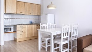 A kitchen with wooden cabinets, a white dining table with chairs, a white refrigerator, and a hanging light fixture. -  RVApartaments Club Torrevella (Torroella de Montgrí)