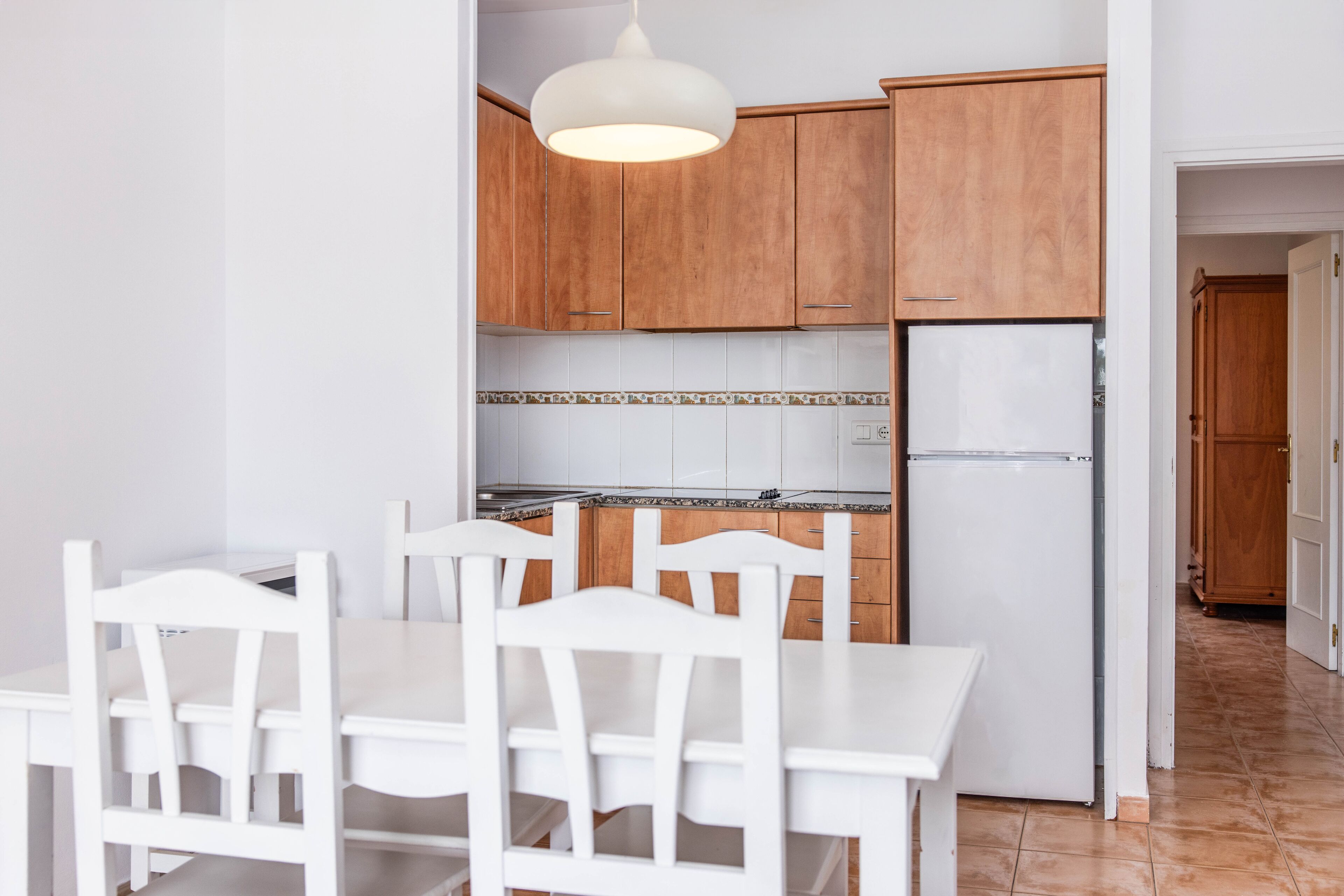 A kitchen with wooden cabinets, a white refrigerator, and a dining table with chairs.