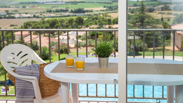 A balcony with a table, two glasses of orange juice, a potted plant, and a chair with a striped pillow. -  RVApartaments Club Torrevella (Torroella de Montgrí)