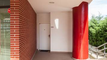 Un pasillo con un pilar rojo, una puerta con la etiqueta 'A01' y vistas al exterior con vegetación.