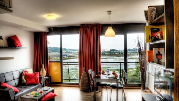 Un salon moderne avec un canapé, une table à manger et des chaises. Une grande fenêtre offre une vue sur une rivière et sur la verdure.