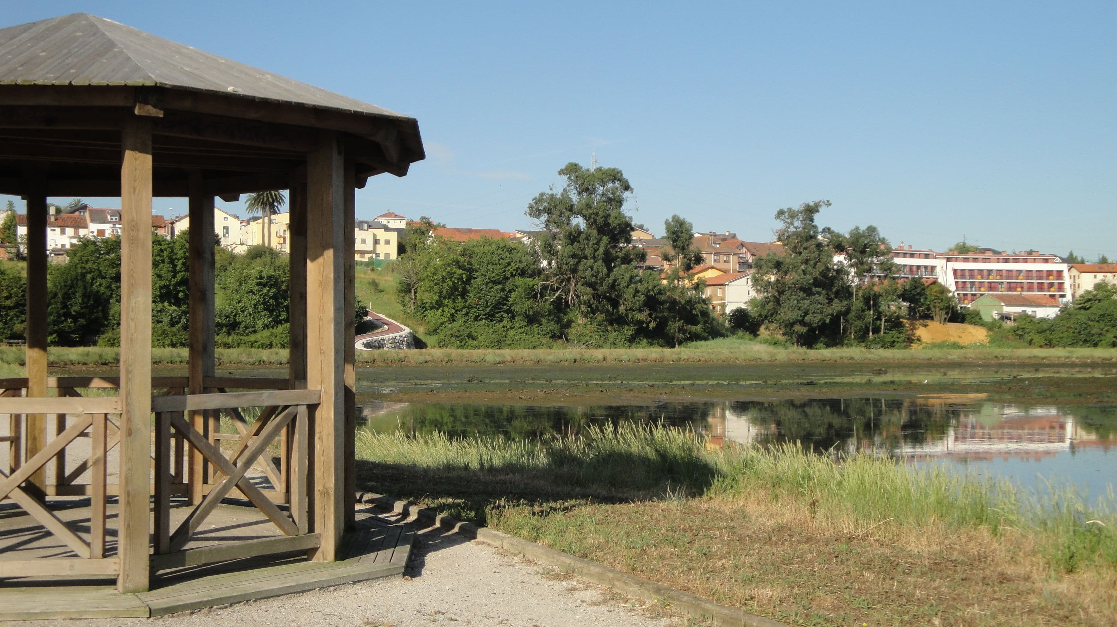 Un gazebo in legno affacciato su un lago tranquillo, con vista sulle abitazioni sullo sfondo.