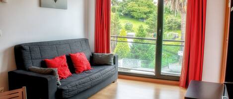 Una sala de estar moderna con un sofá gris, cojines rojos, una mesa de madera y un ventanal con cortinas rojas.