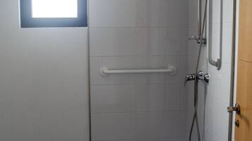 Un espacio de ducha pequeño y cerrado, con ventana, barra de apoyo y cabezal de ducha.