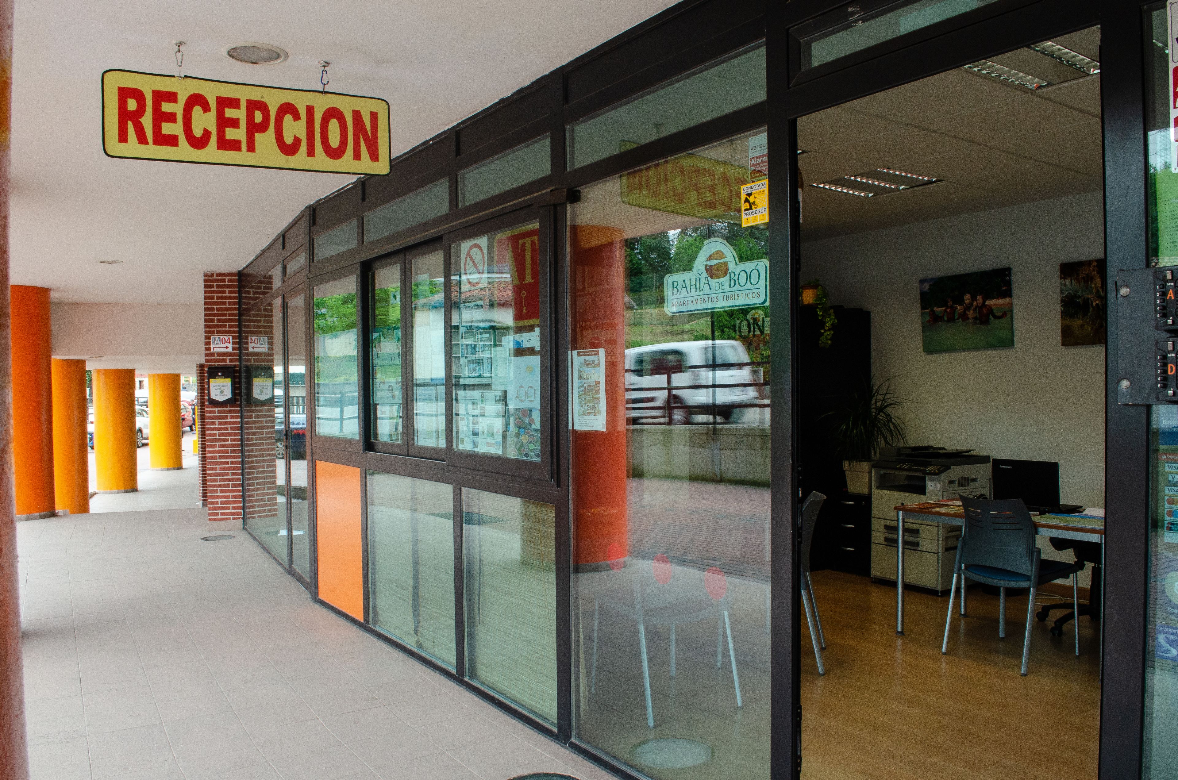 Un espace d’accueil avec une enseigne indiquant « RÉCEPTION », une porte d’entrée en verre et un bureau visible avec un bureau et des chaises.