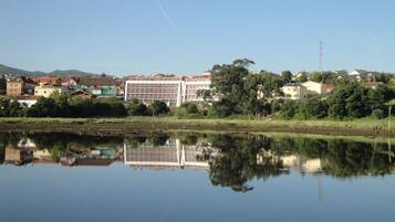 A riverside view with a modern building reflecting on the water, surrounded by trees and other residential buildings.