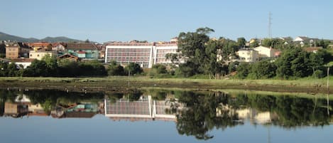 Vista de riu amb un edifici modern reflectit a l'aigua, envoltat d'arbres i altres edificis residencials.
