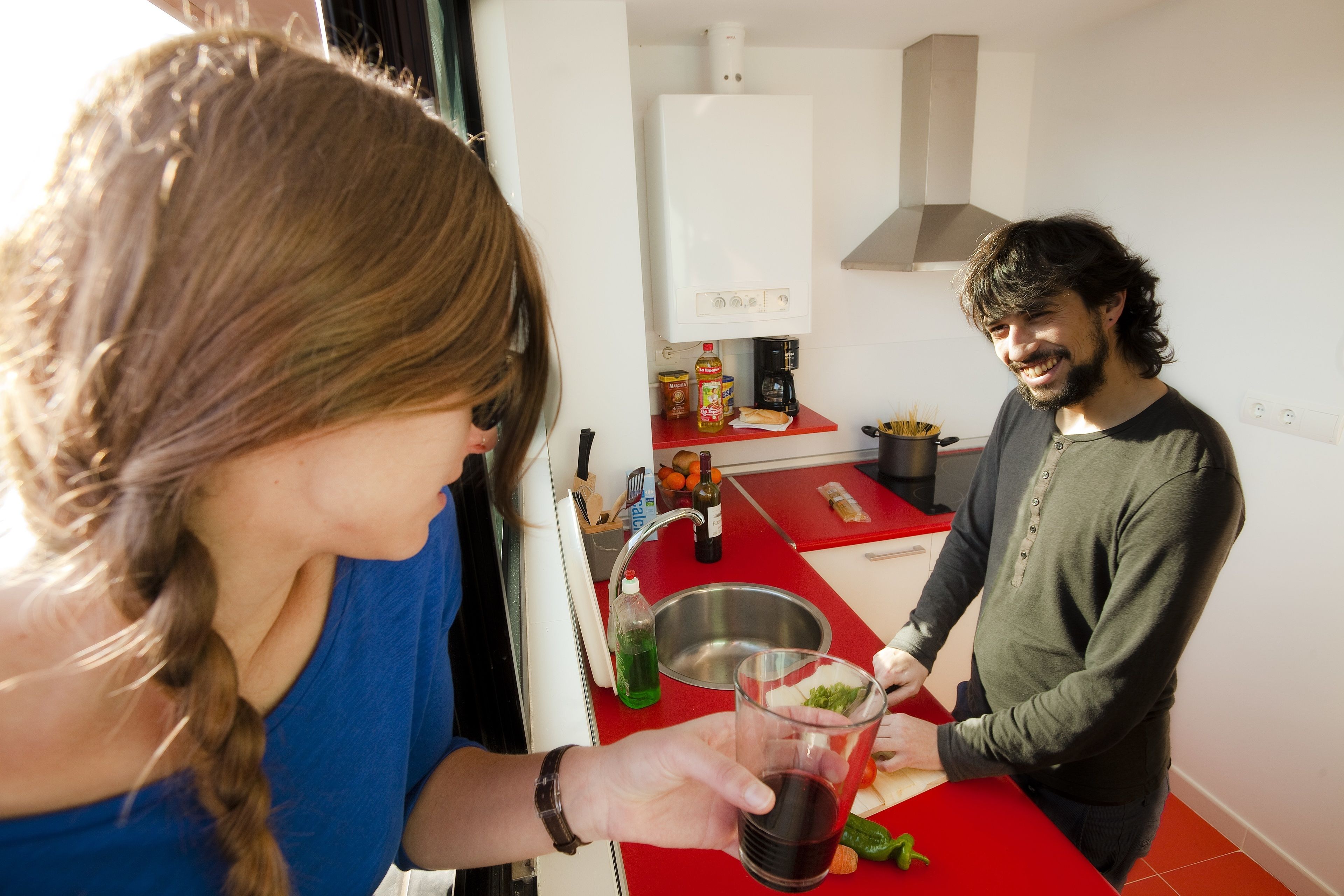 Una cuina moderna amb taulell vermell, vàter d'acer inoxidable i armaris blancs.