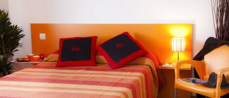 A hotel room with a bed, two pillows, a nightstand, a lamp, a chair, and a plant.