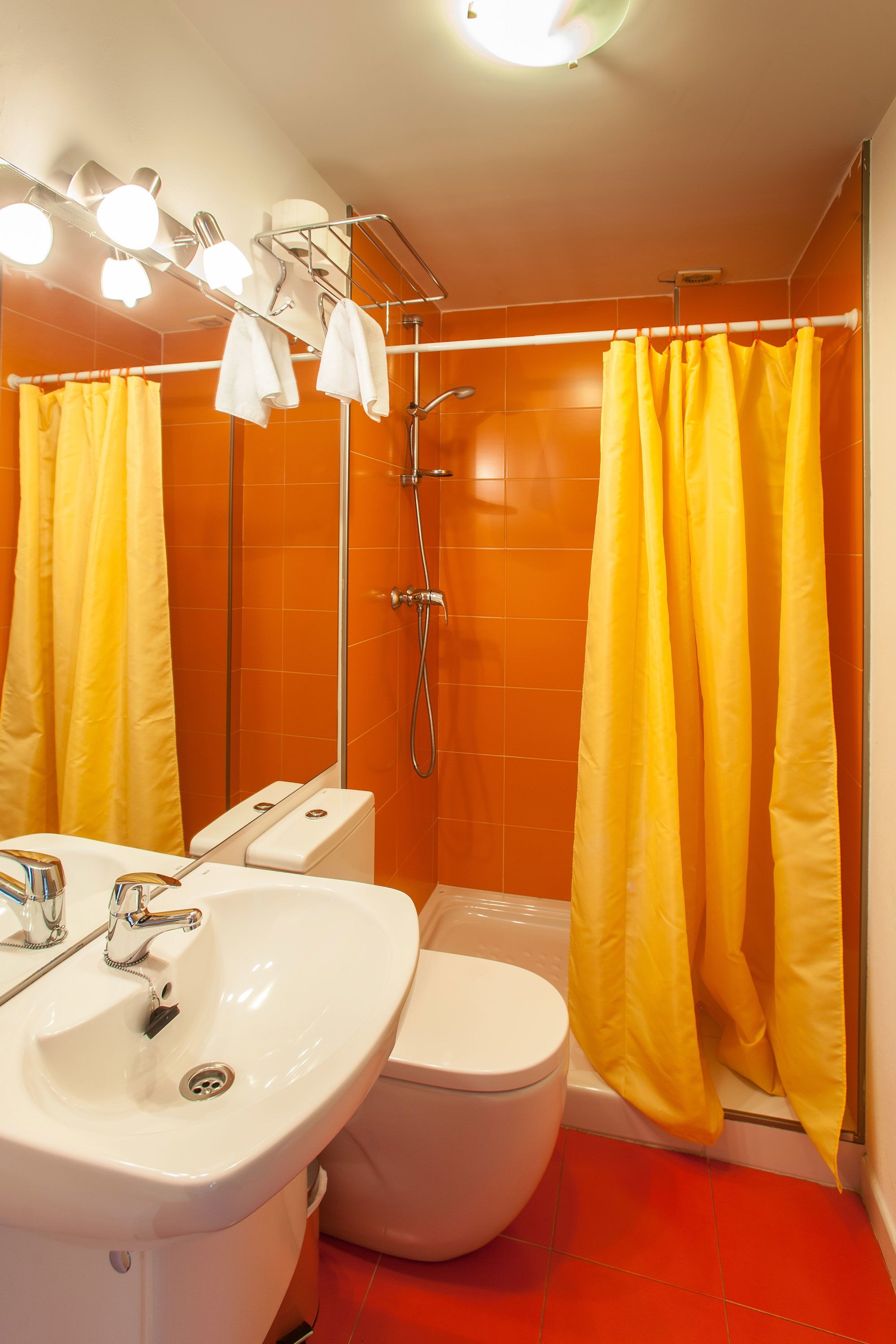 Baño con lavamanos, inodoro y ducha blancos. Hay cortinas amarillas.