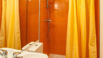 Baño con lavamanos, inodoro y ducha blancos. Hay cortinas amarillas.