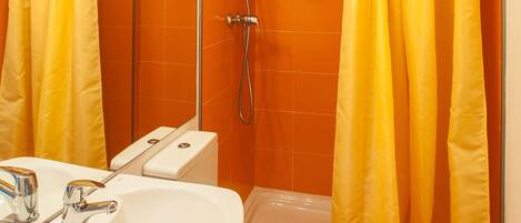 Baño con lavamanos, inodoro y ducha blancos. Hay cortinas amarillas.