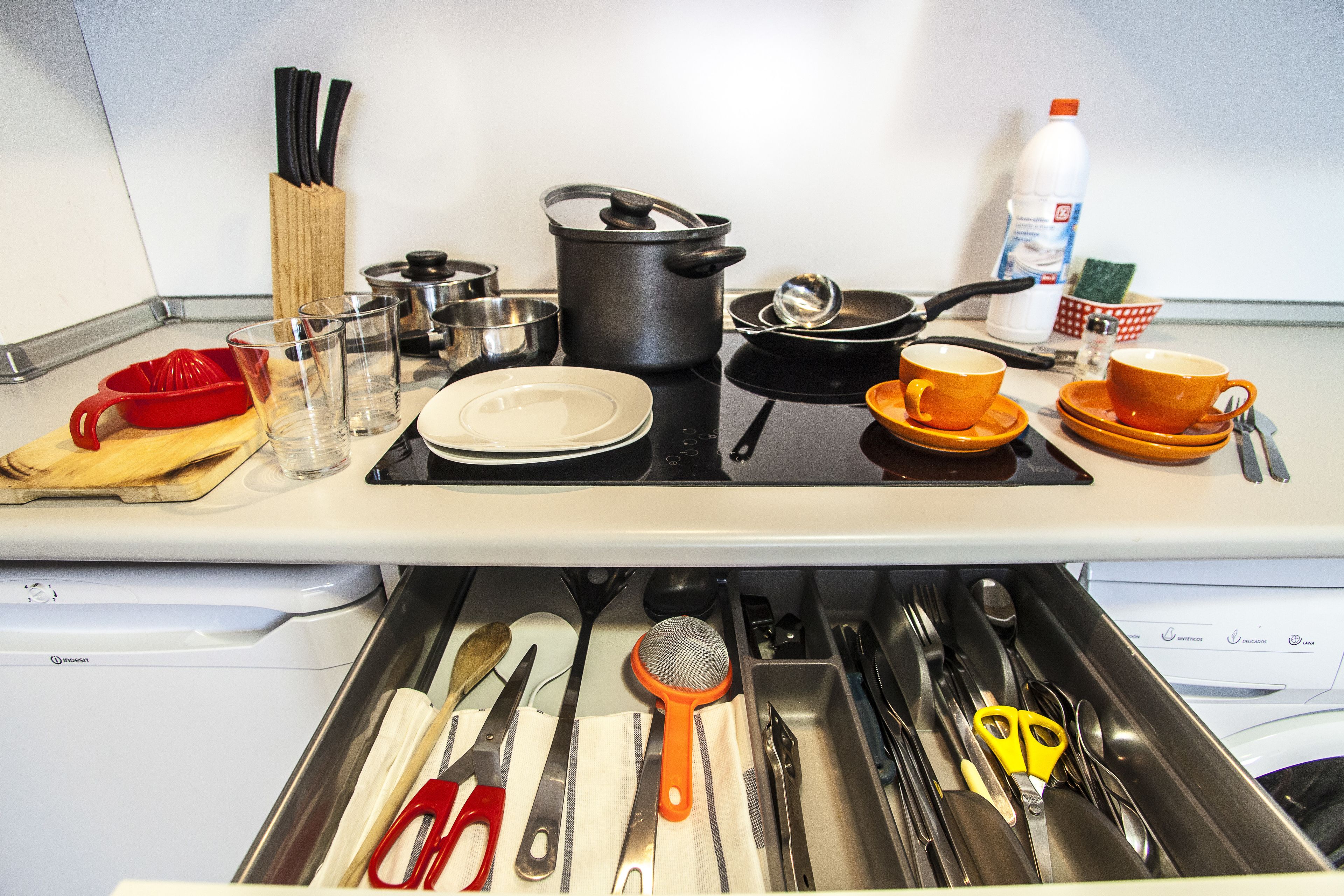 Una cocina con estufa, ollas, sartenes y diversos utensilios.