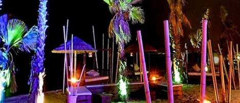 A beach area with palm trees, a thatched-roof structure, and bamboo poles.