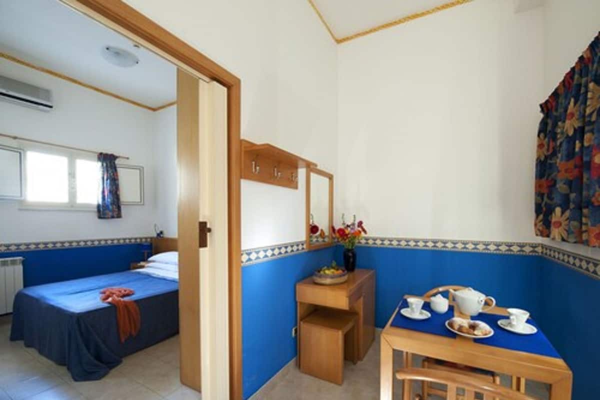 Una habitación con dos camas, una mesita pequeña con una silla, un espejo y una ventana con cortinas.