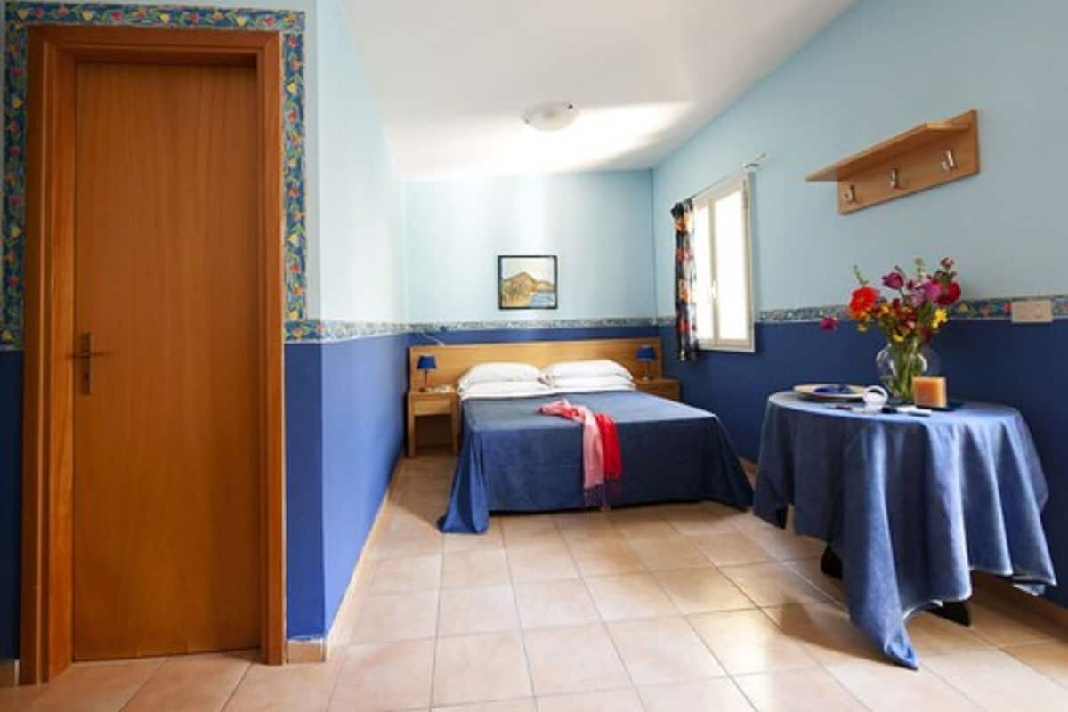 Una habitación con una cama, una mesita de noche con un florero y una ventana.