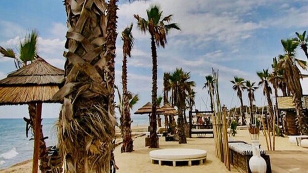 A beach with palm trees, a thatched-roof structure, and a circular seating area. - Villaggio Turistico Internazionale La Plaja (Catania)