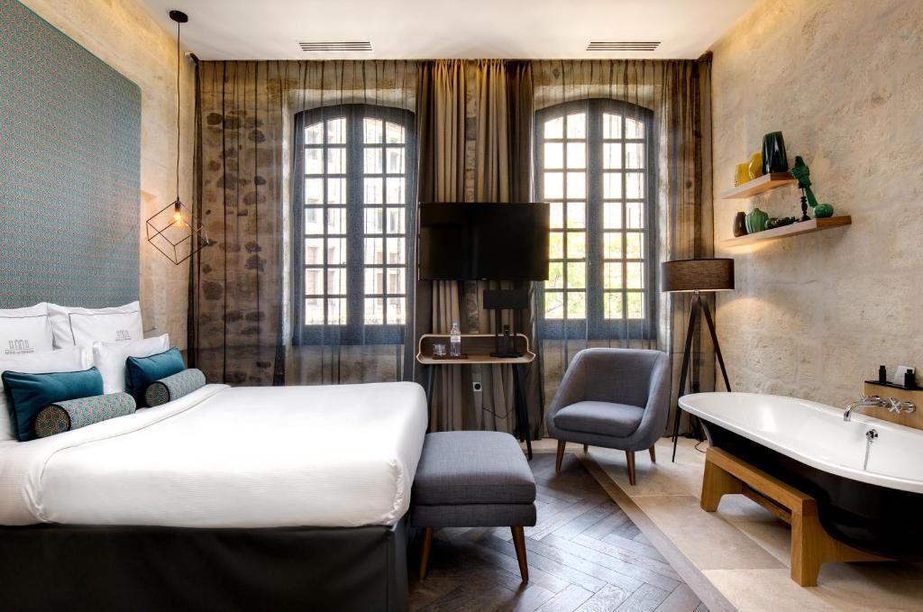 Une chambre d’hôtel comprenant un lit, une chaise, un bureau, une télévision, une étagère avec des articles de toilette et une baignoire.