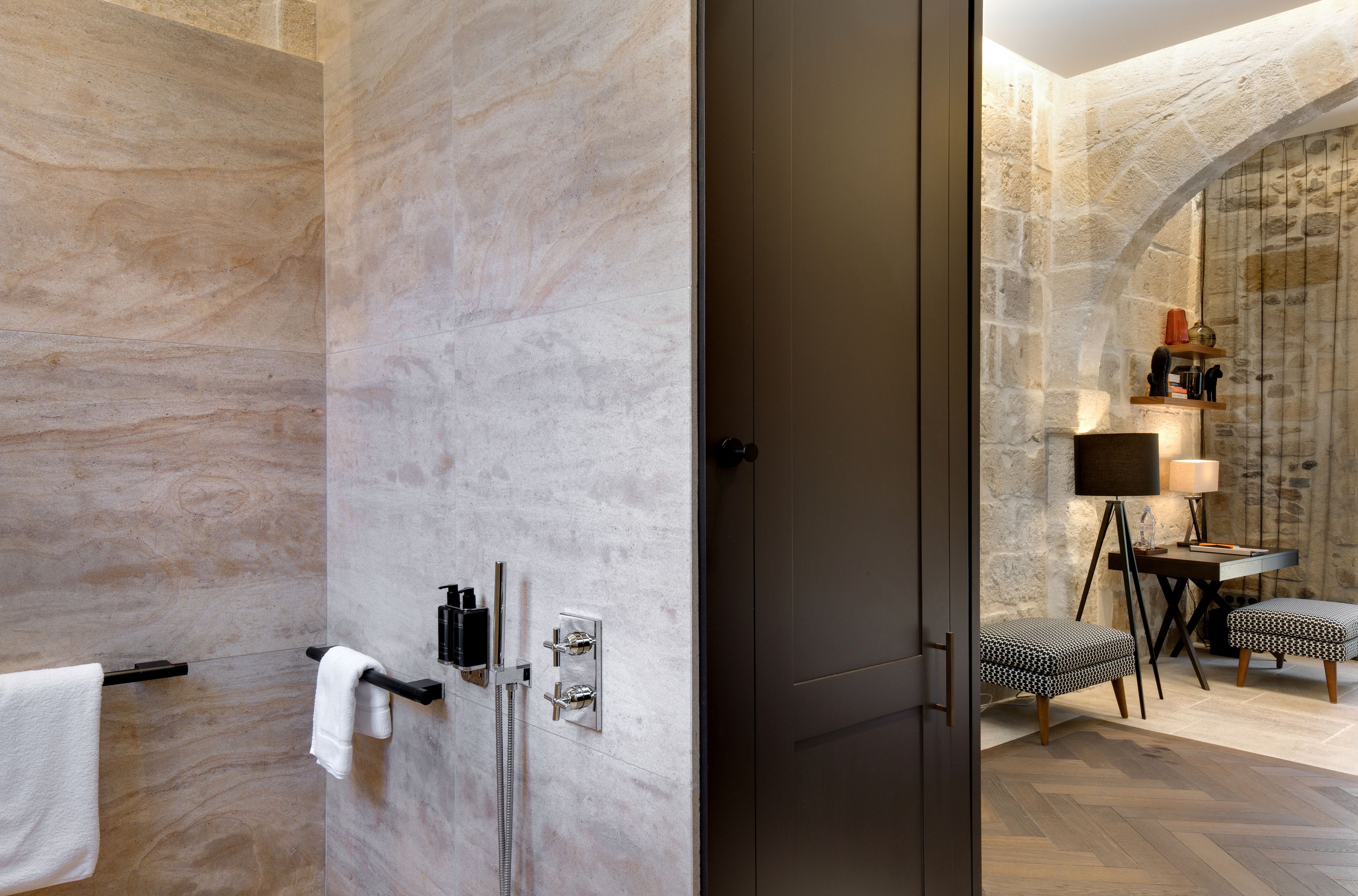 Een moderne badkamer met een marmeren wand, een douche en een zithoek met een tafel en stoelen.