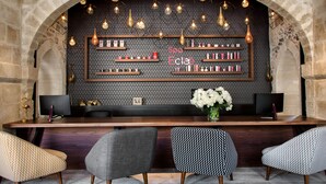 A reception area with a stone arch, a wooden reception desk, multiple shelves with products, and three patterned chairs. - Boutique Hôtel des Remparts (Aigues-Mortes)