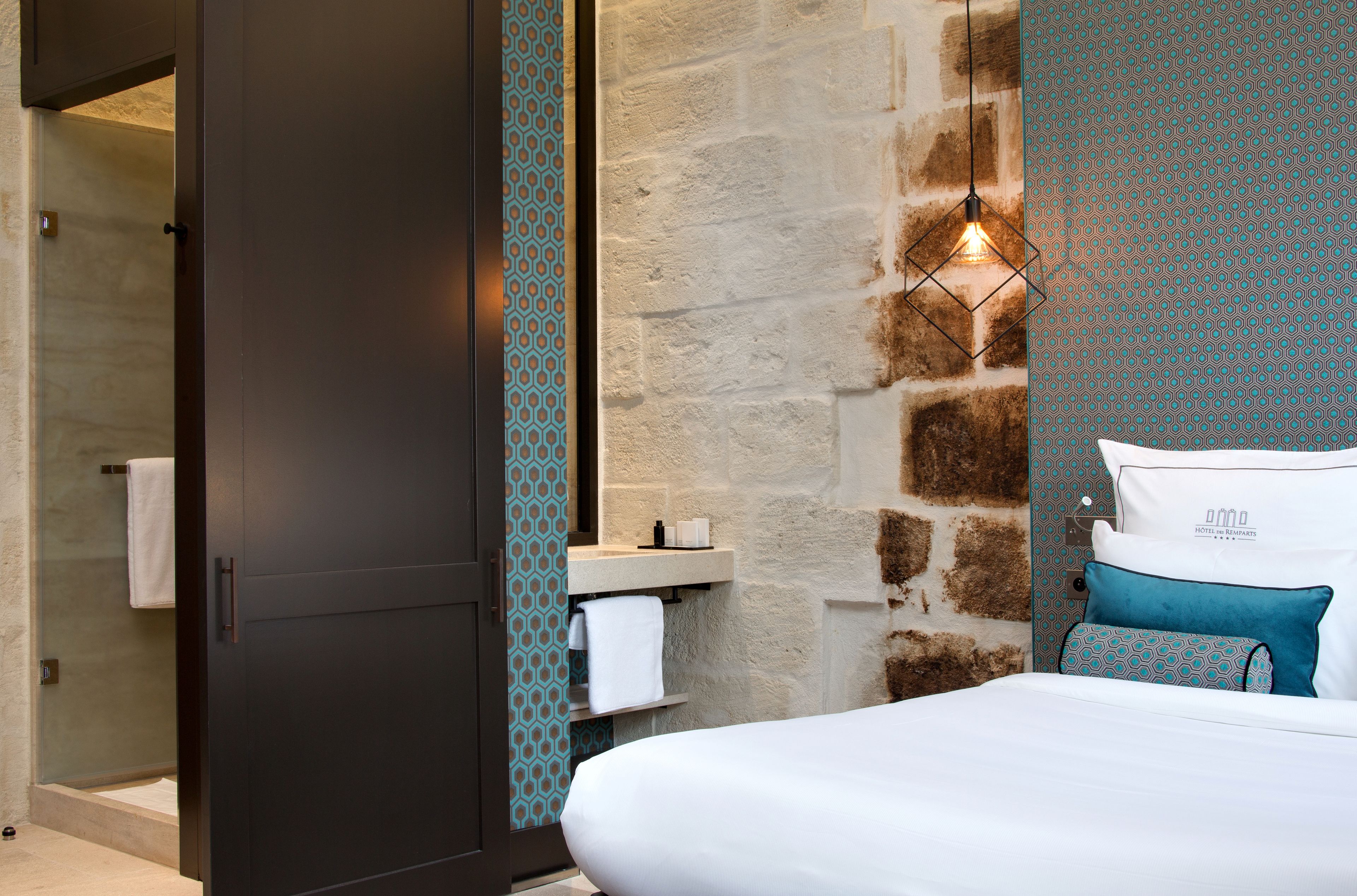 Una habitación de hotel moderna con una cama grande, un armario oscuro, un baño con ducha y una pared con diseño.