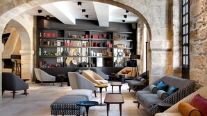 A spacious living area with modern furniture, a large bookshelf, and stone arches. - Boutique Hôtel des Remparts (Aigues-Mortes)