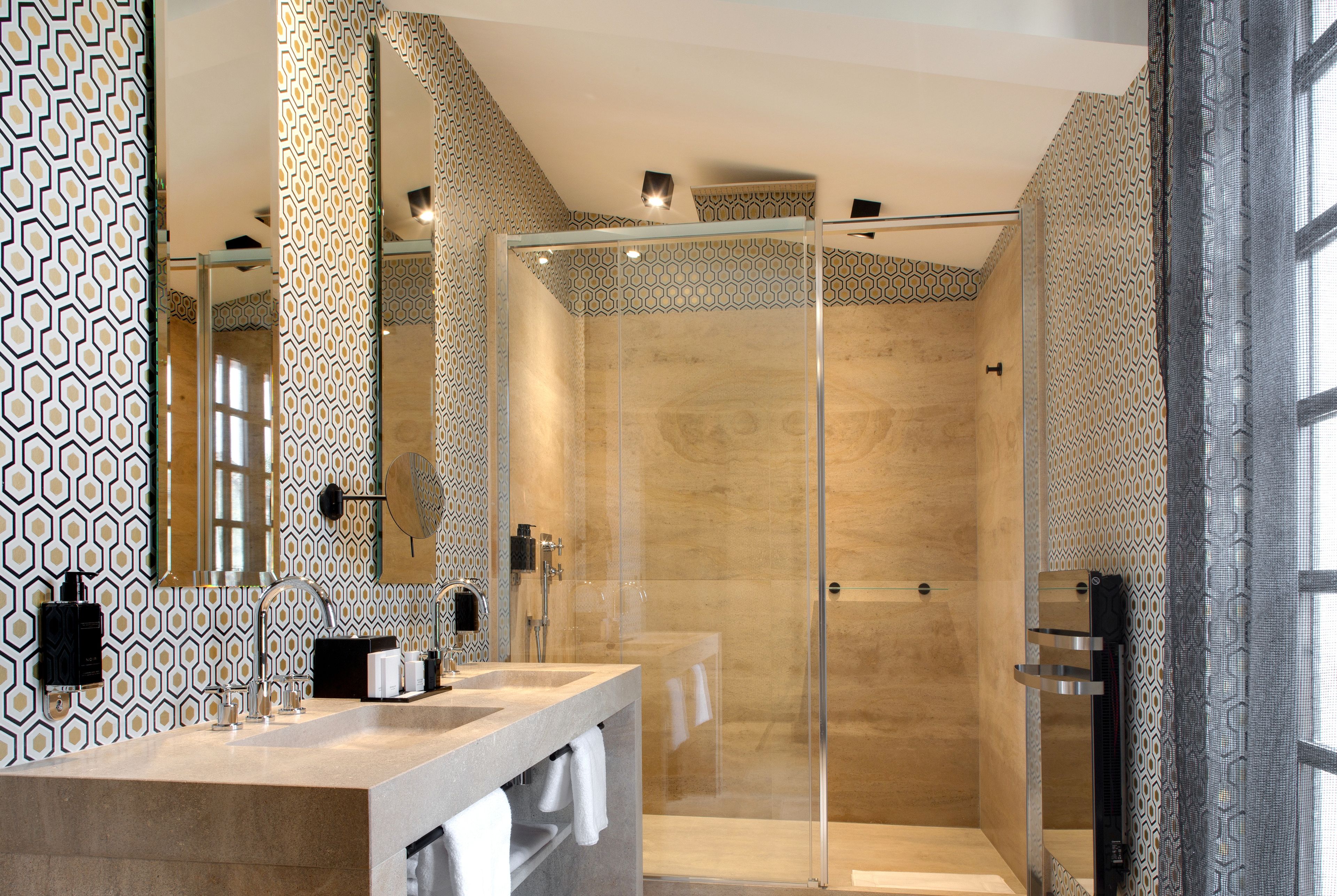 A modern bathroom with a large mirror, a glass-enclosed shower, and patterned walls.
