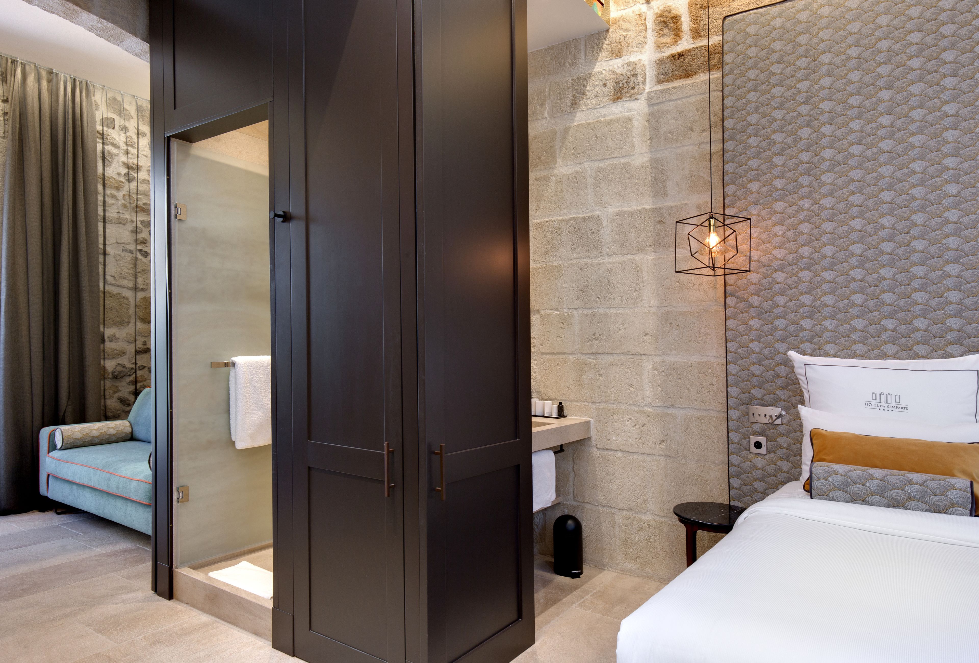 Una habitación de hotel moderna con ducha de vidrio, un sofá, una cama con cabecera y una mesita de noche pequeña.