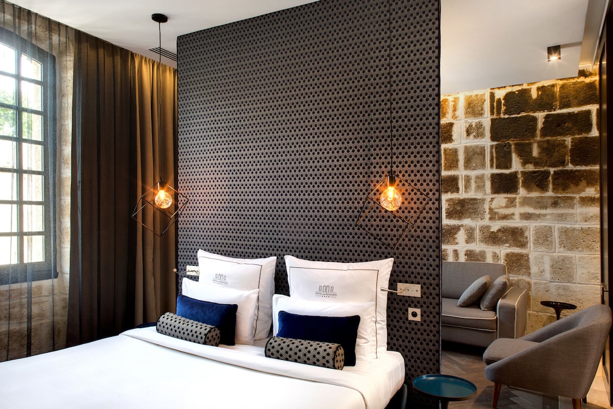 A modern hotel room with a large bed, two bedside tables, a sofa, and a stone accent wall.