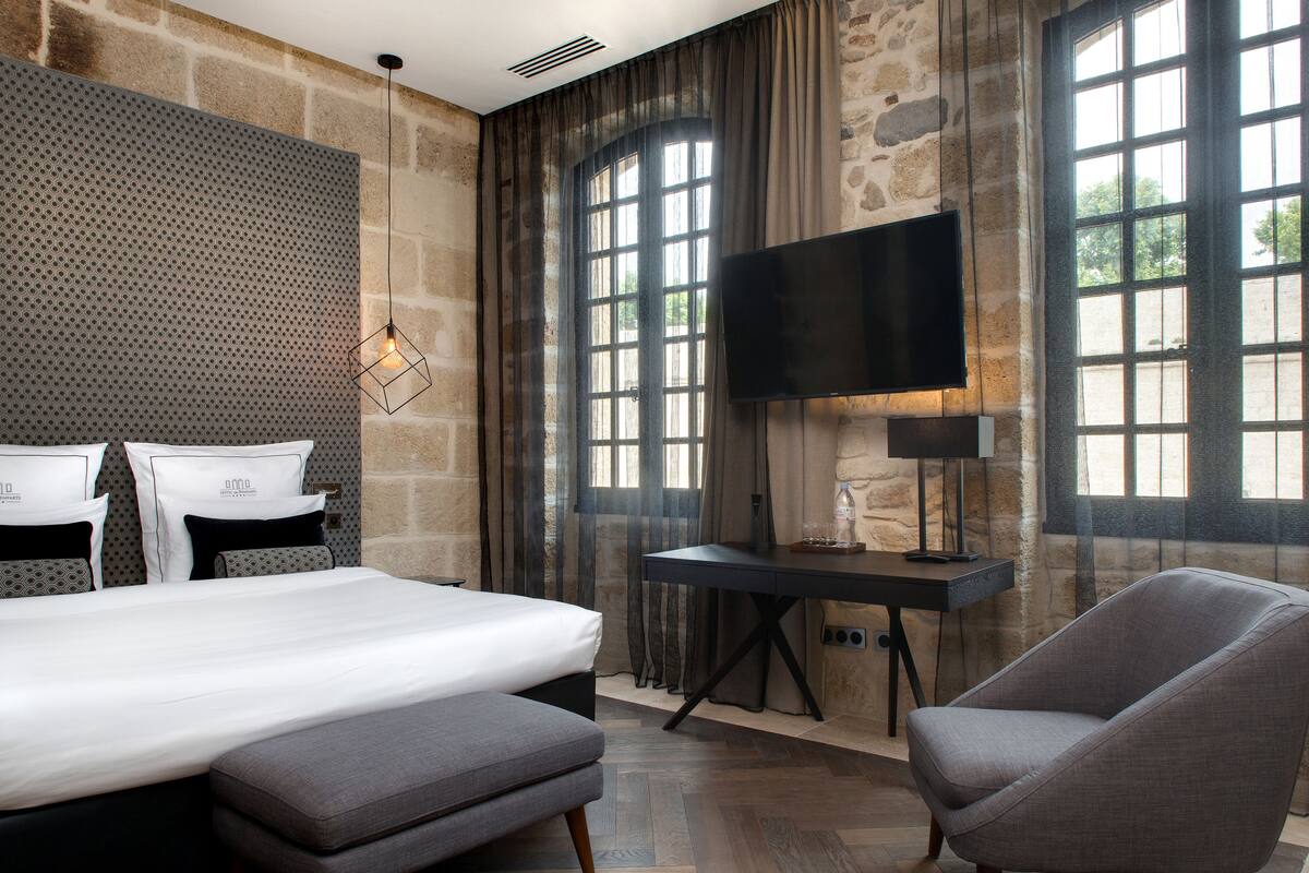 A modern hotel room with a large bed, a desk, a chair, and a TV.